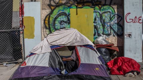 A homeless man sits in his tent as anofher sleeps on the sidewalks in front of the non-profit Midnight Mission's headquarters, while traditional Thanksgiving meals are served to nearly 2000 homeless people in the Skid Row neighborhood of downtown Los Angeles on November 25, 2021. (Photo by Apu GOMES / AFP) (Photo by APU GOMES/AFP via Getty Images)