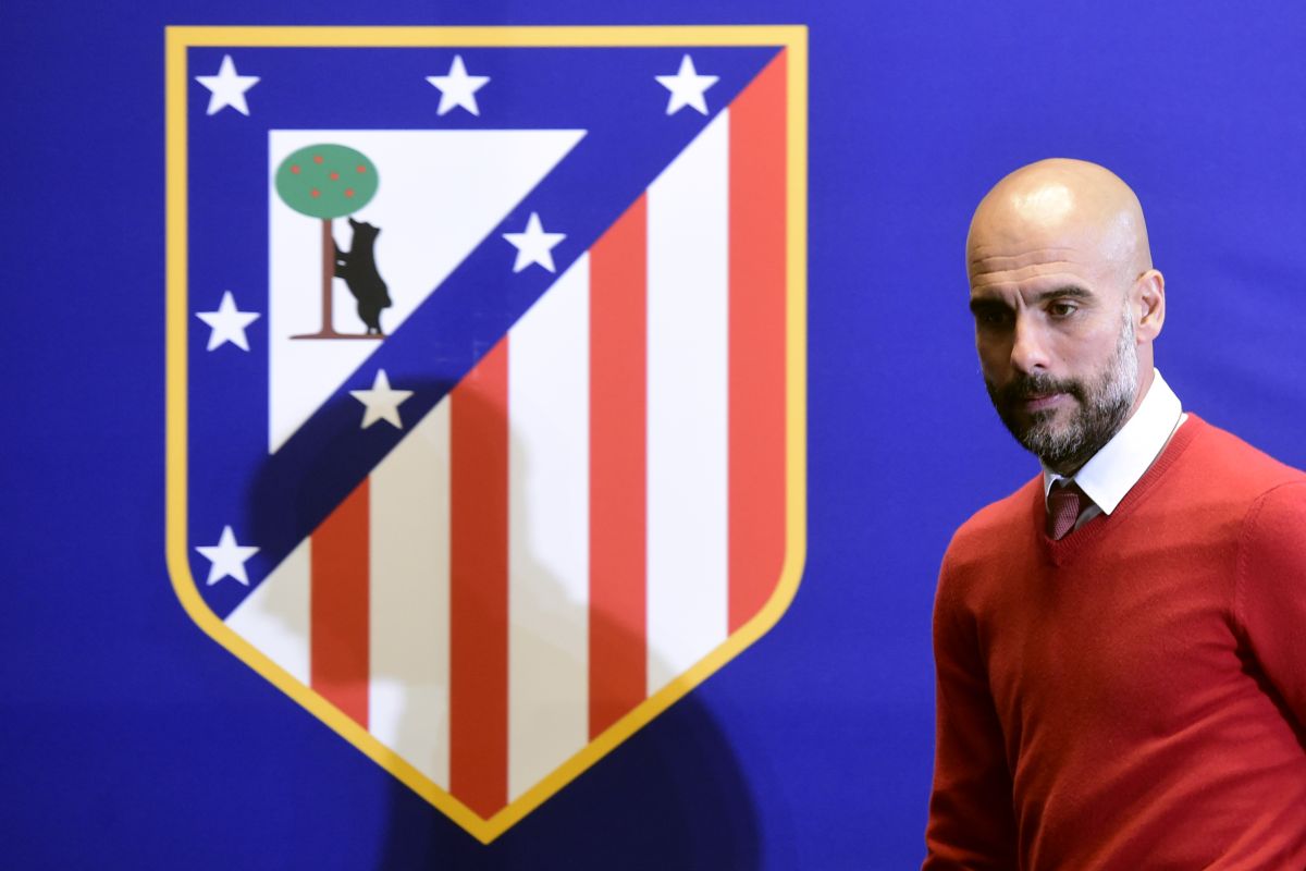 Pep Guardiola junto al escudo que utilizó el Atlético de Madrid entre 1947 y el 2017.