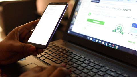 A woman uses a smartphone in front of a laptop on April 3, 2019, in Abidjan. - According to the figures of the platform of the fight against cybercrime (PLCC) of the national police, nearly one hundred crooks of the internet, were arrested in 2018 in Ivory Coast, a country known for its scammers on the web, has announced on April 2, 2019 the Ivorian authority of regulation of the telephony. (Photo by ISSOUF SANOGO / AFP) (Photo by ISSOUF SANOGO/AFP via Getty Images)