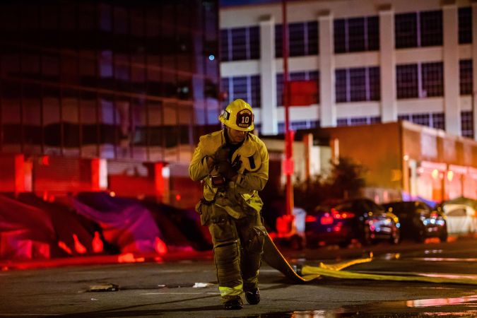 A firefighter drags a hose on San Pedro Street after a fire in a single-story commercial building sparked an explosion in the Toy District of downtown Los Angeles on May 16, 2020. - At least 11 firefighters were injured in downtown Los Angeles when a fire in a commercial building sparked a major explosion and spread to nearby structures, fire officials said. Some 230 responders battled the blaze as it spread to other buildings in the area before it was extinguished around two hours after it began. (Photo by Apu GOMES / AFP) (Photo by APU GOMES/AFP via Getty Images)