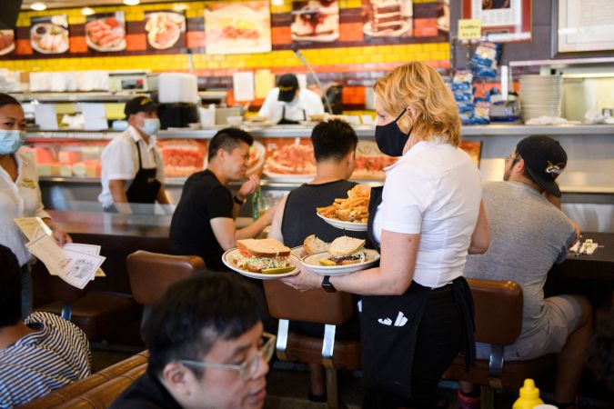 A waiter serves food to customers dining indoors at Langer's Deli in Los Angeles, California on August 7, 2021. - The restaurant announced that proof of vaccination would be required to dine indoors at the restaurant as Covid-19 variant causes surge in the Los Angeles area. (Photo by Patrick T. FALLON / AFP) (Photo by PATRICK T. FALLON/AFP via Getty Images)