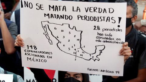 Un periodista sostiene un cartel que dice:"matando periodistas no se mata la verdad" durante una protesta.