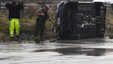 A Los Angeles County Sheriffs Department deputy (C) and California Highway Patrol officer (L) look at a flipped vehicle in the rain on Interstate 5 during a winter storm near Gorman, California, on March 21, 2023. (Photo by Patrick T. Fallon / AFP) (Photo by PATRICK T. FALLON/AFP via Getty Images)