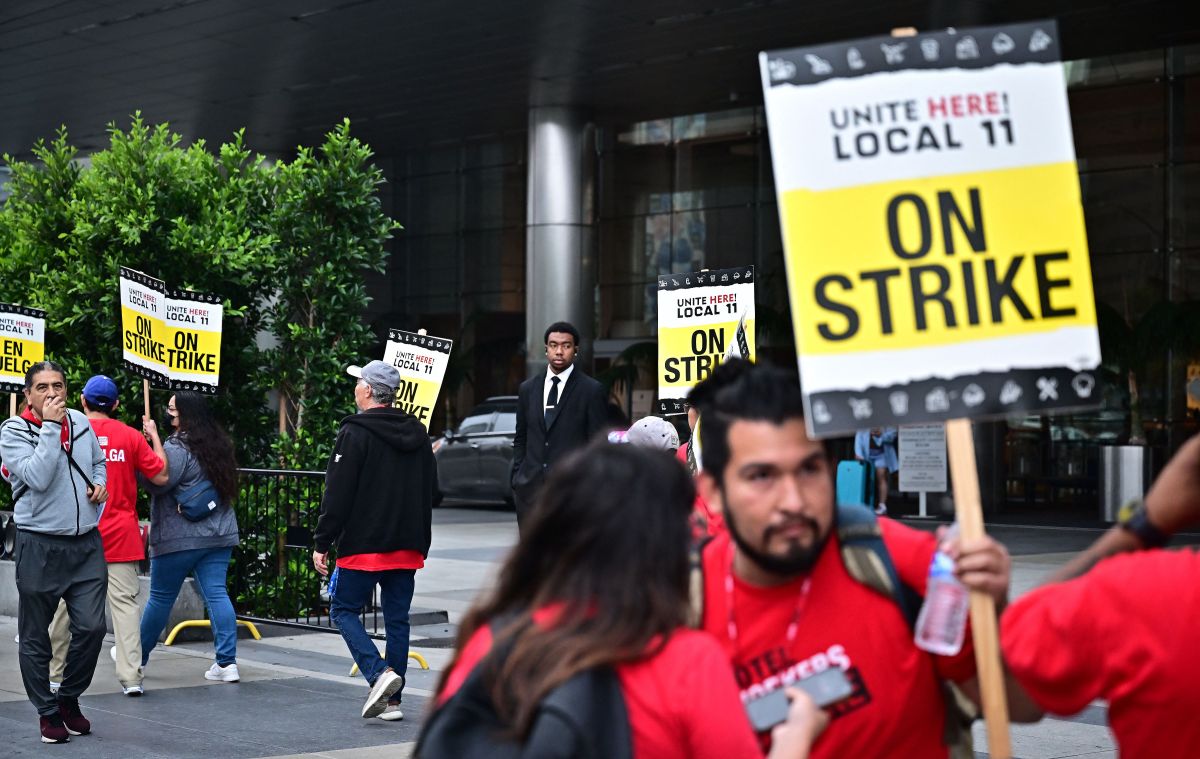A security guards watches as hotel workers hold placards during the second day on their strike for a better wage in front of the JW Marriot Hotel on July 3, 2023 in Los Angeles, California. Contracts between UNITE HERE Local 11 and 61 hotels expired at midnight on Friday, June 30. (Photo by Frederic J. BROWN / AFP) (Photo by FREDERIC J. BROWN/AFP via Getty Images)