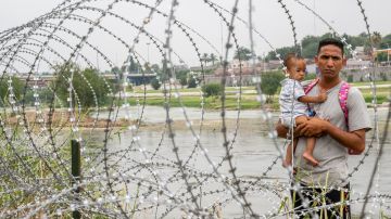 Una familia que busca asilo mira a través de la cerca de alambre de púas después de cruzar ilegalmente el Río Grande hacia Estados Unidos el 14 de junio de 2023 en Eagle Pass, Texas.