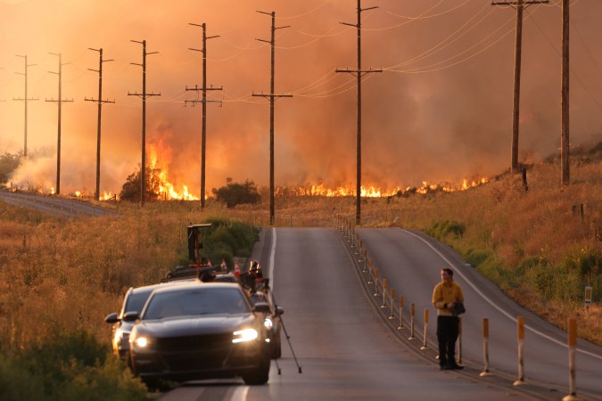 A man stands in a road near flames of the Rabbit fire in Moreno Valley in Riverside County, Californian on July 14, 2023. Tens of millions of Americans were facing dangerously high temperatures July 14, 2023 as a powerful heat wave stretched from California to Texas, with its peak expected this weekend. A heat dome has been baking the southwestern states all week, posing serious health risks to the elderly, construction workers, delivery workers and the homeless. (Photo by DAVID SWANSON / AFP) (Photo by DAVID SWANSON/AFP via Getty Images)
