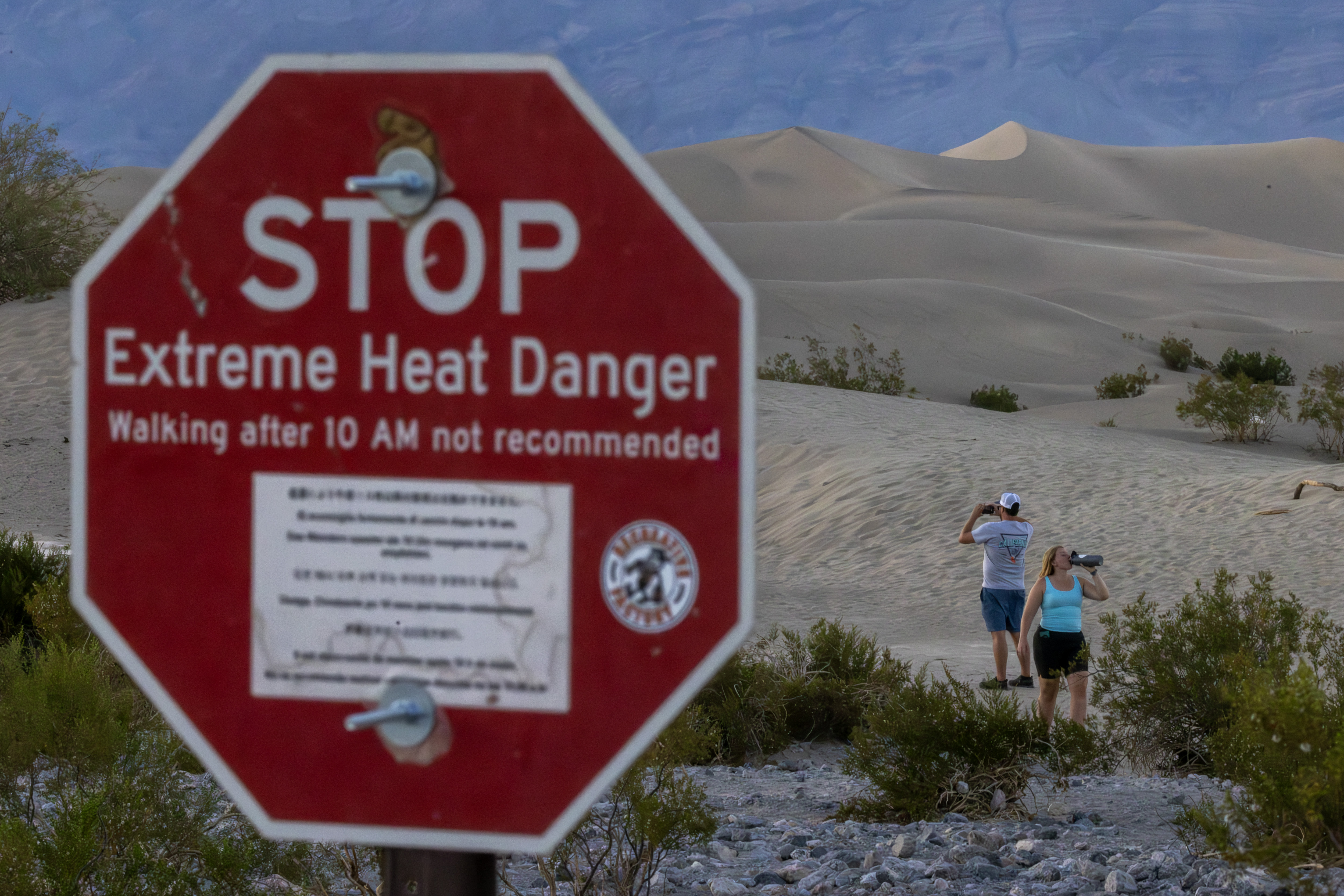 FURNACE CREEK, CALIFORNIA - JULY 15: A woman drinks among sand dunes near a sign warning of extreme heat danger on the eve of a day that could set a new world heat record in Death Valley National Park on July 15, 2023 near Furnace Creek, California. Weather forecasts for tomorrow call for a high temperature of 129º Fahrenheit and possibly as high as 131. Previously, the highest temperature reliably recorded on Earth was 129.2F (54C) in Death Valley in 2013. A century earlier a high temperature in Death Valley reportedly reached 134F but many modern weather experts have rejected that claim along with other high summer temperatures reported in the region that year. (Photo by David McNew/Getty Images)