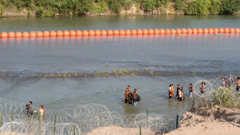 Migrantes caminan junto al muro de boyas colocadas en la frontera de Río Grande con México en Eagle Pass, Texas, el 16 de julio de 2023.