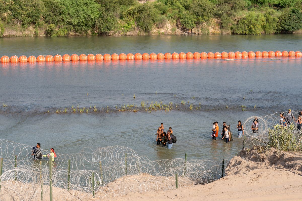 Migrantes caminan junto al muro de boyas colocadas en la frontera de Río Grande con México en Eagle Pass, Texas, el 16 de julio de 2023.