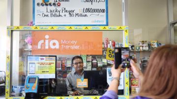 LOS ANGELES, CALIFORNIA - JULY 20: A person poses for a photo beneath an enlarged symbolic check for $1.08 billion in Las Palmitas Mini Market on July 20, 2023 in Los Angeles, California. The $1.08 billion winning Powerball ticket was sold at the Las Palmitas Mini Market for the July 19th drawing. The jackpot is the third largest in Powerball history and was picked after three months of drawings without a winner. The mini market is located in the downtown Fashion District close to Skid Row. (Photo by Mario Tama/Getty Images)