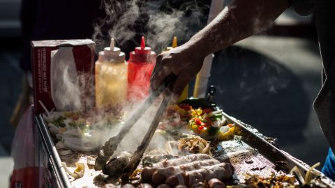 A street vendor prepares hot dogs on a sidewalk off N Main street, in front of Placita Olvera, Downtown Los Angeles on March 10, 2019. - On January 1, 2019, the Safe Vending Act (SB946) went into effect in the state of California prohibiting the arrest or finning of street vendors and leaving to municipalities the power to establish permits, sanitation and security issues. The Los Angeles County has set a year to negotiate with vendors the terms on which the law is going to be applied. Some 50,000 street vendors are estimated to work in Los Angeles, a $504 million industry according to a 2015 study by the Economic Roundtable. The LA County issued a municipal ordinance that designates specific areas where the vendors must operate. The ordinance does not include areas such as Memorial Coliseum, the Staples Center, Dodger Stadium, Rose Bowl Stadium and the Hollywood Walk of Fame. Street vendors have mixed feelings about the legalization of their work. At the same time they feel freed of being against the law and harassed by police giving them tickets and seizing their goods; they are concerned about having to abide to health regulations, permits and limited areas. (Photo by Agustin PAULLIER / AFP) (Photo credit should read AGUSTIN PAULLIER/AFP via Getty Images)