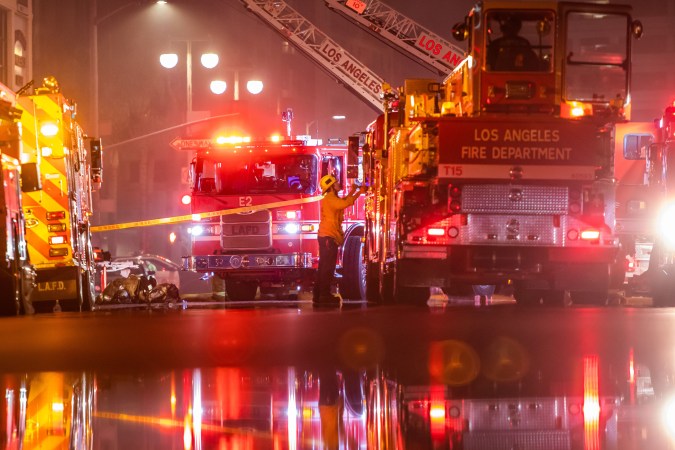 Firefighters gather near firetrucks after a fire in a single-story commercial building sparked an explosion in the Toy District of downtown Los Angeles on May 16, 2020. - At least 11 firefighters were injured in downtown Los Angeles when a fire in a commercial building sparked a major explosion and spread to nearby structures, fire officials said. Some 230 responders battled the blaze as it spread to other buildings in the area before it was extinguished around two hours after it began. (Photo by Apu GOMES / AFP) (Photo by APU GOMES/AFP via Getty Images)