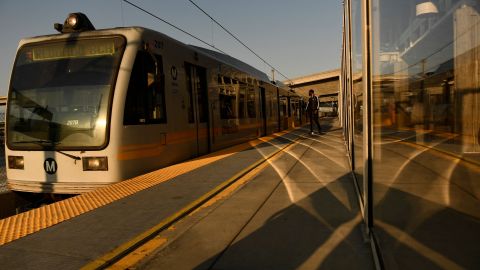 Transit passengers wear face masks as they wait to board the Metro C Line, formerly Green Line, light rail train alongside the 105 Freeway at the Judge Harry Pregerson Interchange during rush hour traffic in Los Angeles, California on July 16, 2021. - The Metro C Line will eventually merge with the Crenshaw/LAX Transit Project as infrastructure modernization and transit construction projects continue at the airport ahead of the 2028 Los Angeles Olympics to reduce carbon emissions, traffic, and their impact towards climate change. (Photo by Patrick T. FALLON / AFP) (Photo by PATRICK T. FALLON/AFP via Getty Images)