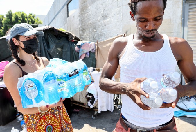 LOS ANGELES, CALIFORNIA - SEPTEMBER 04: A member of the Skid Row community carries away water distributed by volunteers with Water Drop LA on September 4, 2022 in Los Angeles, California. Temperatures hovered around 100 degrees in downtown L.A. amid an intense heat wave in Southern California. Water Drop LA is a mutual aid organization which drops off 2,000 gallons of water each Sunday to members of the Skid Row community, many of who are suffering from water insecurity. Skid Row is home to thousands of people who either live on the streets or in shelters. The National Weather Service issued an Excessive Heat Warning for most of Southern California through September 7. Climate models almost unanimously predict that heat waves will become more intense and frequent as the planet continues to warm. (Photo by Mario Tama/Getty Images)