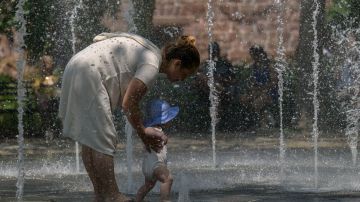 Awoman and her baby cool off in a public fountain at a park as temperatures begin to rise on July 26, 2023 in New York. (Photo by ANGELA WEISS / AFP) (Photo by ANGELA WEISS/AFP via Getty Images)