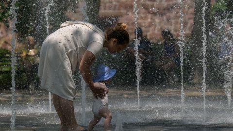 Awoman and her baby cool off in a public fountain at a park as temperatures begin to rise on July 26, 2023 in New York. (Photo by ANGELA WEISS / AFP) (Photo by ANGELA WEISS/AFP via Getty Images)