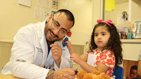 El doctor Fernando Valencia se deja revisar el oído, por parte de una niña de Hope Street Elementary Center.