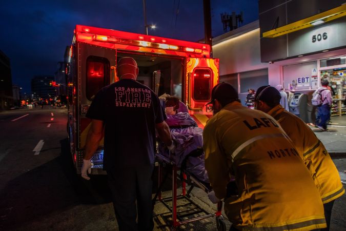 TOPSHOT - Paramedics of the LAFD Station No9 wear a face mask as a preventive measure against the spread of the COVID-19 novel coronavirus from a homeless woman who had seizures on the street at Skid Row, before boarding her in the ambulance to go to a hospital on April 12, 2020 in downtown Los Angeles, California. - One of the busiest fire station in the country , LA Fire Station 9 is on the front lines of California's homeless crisis e Coronavirus pandemic. (Photo by Apu GOMES / AFP) (Photo by APU GOMES/AFP via Getty Images)