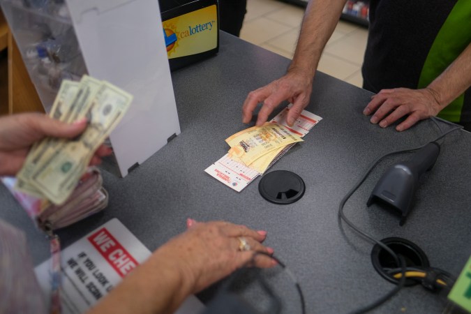 People buy their Mega Millions lottery tickets at a 7-Eleven convenience store in Chino Hills, California, July 28, 2022. - The odds of claiming this week's bonanza US lottery prize are less than one-in-300-million -- but one "lucky" convenience store outside Los Angeles is already counting its winnings. A sign above the counter of the otherwise unassuming shop in California's Chino Hills proclaims itself the "LUCKIEST 7-ELEVEN IN THE WORLD," six years after it sold a winning ticket for the largest jackpot in US lottery history. (Photo by RINGO CHIU / AFP) (Photo by RINGO CHIU/AFP via Getty Images)