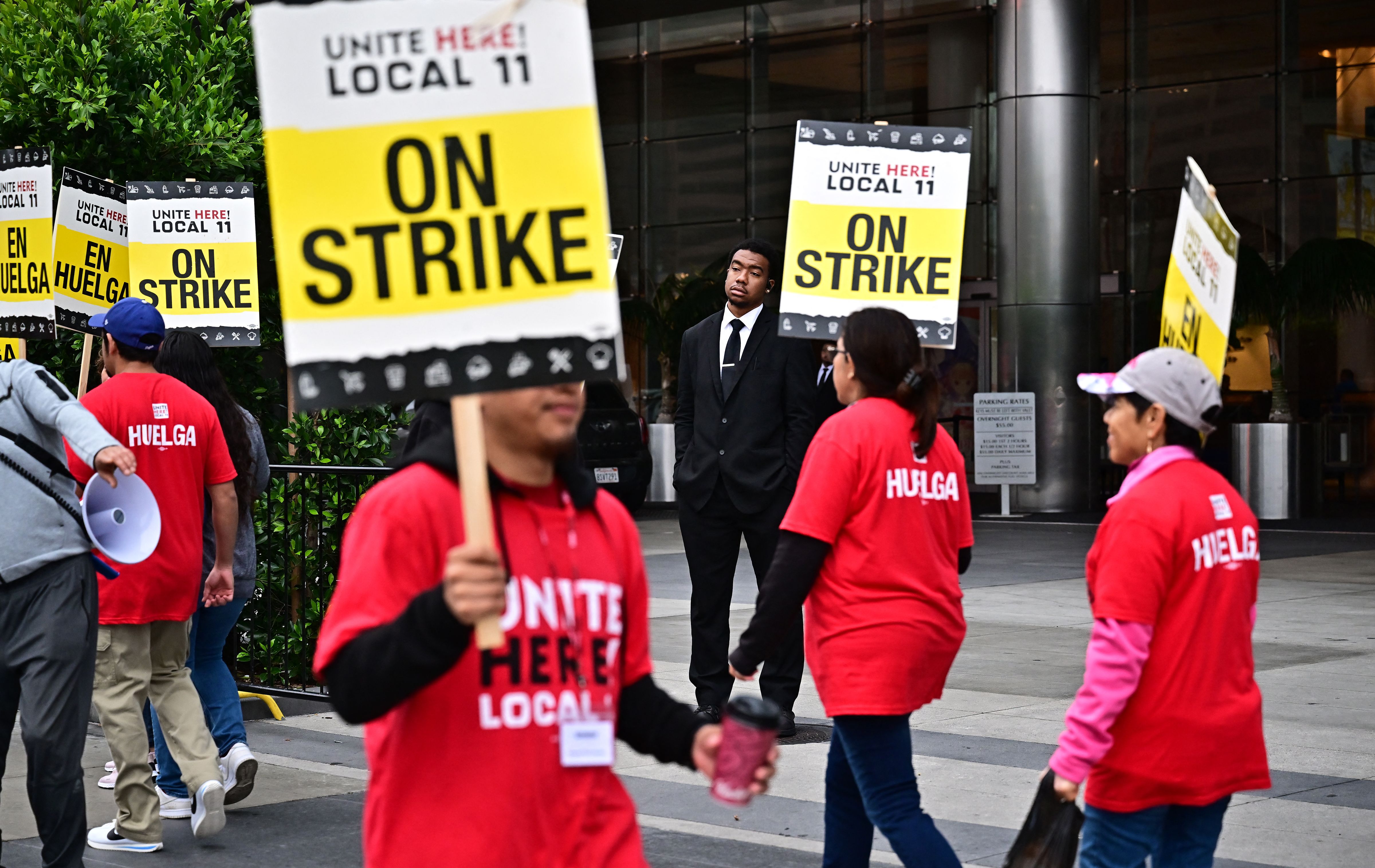 A security guards watches as hotel workers hold placards during the second day on their strike for a better wage in front of the JW Marriot Hotel on July 3, 2023 in Los Angeles, California. Contracts between UNITE HERE Local 11 and 61 hotels expired at midnight on Friday, June 30. (Photo by Frederic J. BROWN / AFP) (Photo by FREDERIC J. BROWN/AFP via Getty Images)