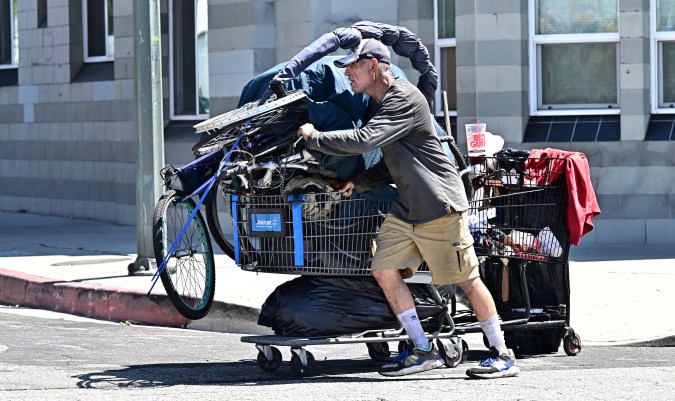 A homeless man pushes his belongings across a street on August 16, 2023 in the Skid Row neighborhood of Los Angeles, California, where homelessness has seen a 10 percent surge compared to last year. A recent report from the Los Angeles Homeless Services Authority reveals an estimate of 42,260 people living on the streets of Los Angeles without shelter, as the homeless population has more than doubled over the past decade. (Photo by Frederic J. BROWN / AFP) (Photo by FREDERIC J. BROWN/AFP via Getty Images)