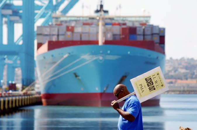 LONG BEACH, CA - SEPTEMBER 30: A dock worker carrying a sign that reads "Locked Out" walks past a ship docked at the Port of Los Angeles left partially loaded with shipping containers during the indefinite lockout of longshoremen by shippers September 30, 2002 in Long Beach, California. The labor dispute that has resulted in the shutdown of the West Coast shipping trade is costing the United States $1 billion per day, about 7 percent of the U.S. gross domestic product. The ports of Los Angeles and Long Beach are the nation's busiest, and the fall months are typically the busiest of the year as retailers stock up on imported goods for the Christmas shopping season. (Photo by David McNew/Getty Images)