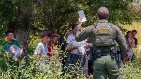 Migrantes que cruzaron desde México en Eagle Pass, Texas escuchan a un agente de CBP.