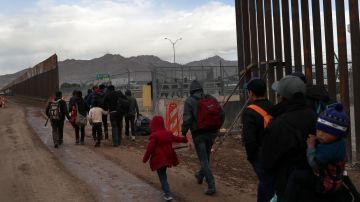 Inmigrantes cruzan por un espacio en la valla fronteriza después de cruzar el Río Grande en El Paso.