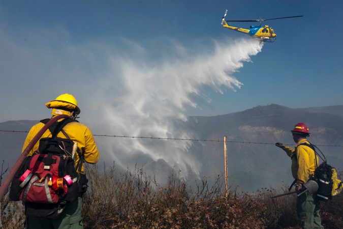 SIMI VALLEY, CA - OCTOBER 30: A firefighting helicopter makes a water drop near firefighters battling the Easy Fire on October 30, 2019 near Simi Valley, California. The National Weather Service issued a rare extreme red flag warning for Southern California for gusts that could be the strongest in more than a decade, exceeding 80 mph, as the fast-moving brush fire threatens the Ronald Reagan Presidential Library and nearby residential neighborhoods. (Photo by David McNew/Getty Images)