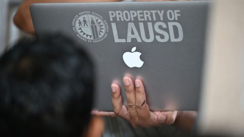 A school administrator confirms student health check data on a laptop computer as students and parents wait in line to enter school grounds on the first day of the school year at Grant Elementary School, in Los Angeles, California on August 16, 2021. - To stem the spread of Covid-19 coronavirus teachers in Los Angeles are required to be fully vaccinated against Covid-19 by October 15 and both teachers and students are required to wear masks inside school buildings. Issues wih the new "Daily Pass" health check app caused confusion and long lines on the first day back to school. (Photo by Robyn Beck / AFP) (Photo by ROBYN BECK/AFP via Getty Images)