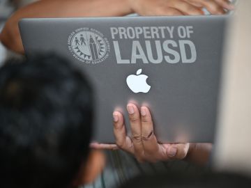 A school administrator confirms student health check data on a laptop computer as students and parents wait in line to enter school grounds on the first day of the school year at Grant Elementary School, in Los Angeles, California on August 16, 2021. - To stem the spread of Covid-19 coronavirus teachers in Los Angeles are required to be fully vaccinated against Covid-19 by October 15 and both teachers and students are required to wear masks inside school buildings. Issues wih the new "Daily Pass" health check app caused confusion and long lines on the first day back to school. (Photo by Robyn Beck / AFP) (Photo by ROBYN BECK/AFP via Getty Images)