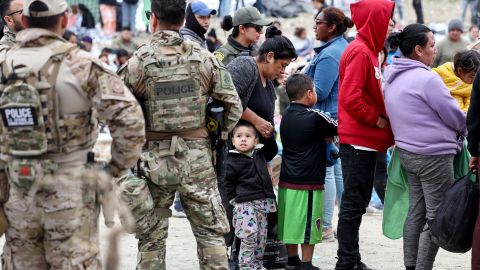 SAN DIEGO, CALIFORNIA - MAY 13: Federal law enforcement agents and officers keep watch as immigrants line up (R) to be transported from a makeshift camp between border walls between the U.S. and Mexico on May 13, 2023 in San Diego, California. Some of the immigrants at the open air camp have been waiting for days in limbo for a chance to plead for asylum while local volunteer groups are providing food and other necessities. The U.S. government's Covid-era Title 42 policy, which for the past three years had allowed for the quick expulsion of irregular migrants entering the country, expired on the evening of May 11. (Photo by Mario Tama/Getty Images)