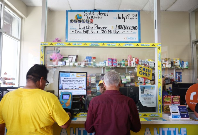 LOS ANGELES, CALIFORNIA - JULY 20: Customers stand beneath an enlarged symbolic check for $1.08 billion in Las Palmitas Mini Market on July 20, 2023 in Los Angeles, California. The $1.08 billion winning Powerball ticket was sold at the Las Palmitas Mini Market for the July 19th drawing. The jackpot is the third largest in Powerball history and was picked after three months of drawings without a winner. The mini market is located in the downtown Fashion District close to Skid Row. (Photo by Mario Tama/Getty Images)