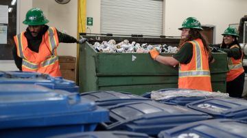 (Izquierda - Derecha) Los trabajadores del Cuerpo de Conservación de Los Ángeles (LACC), Coby Cyrique, Keven Martinez y Diamond Dubon mueven un contenedor de basura lleno de latas en el centro LACC en Los Ángeles, California, el 15 de noviembre de 2023.