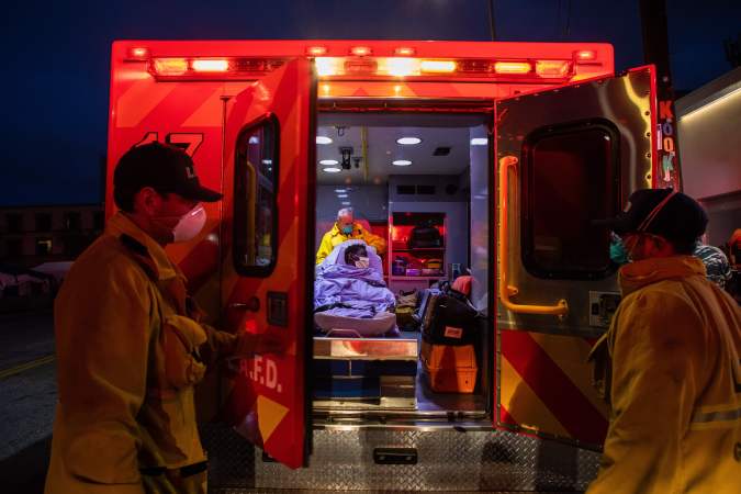 TOPSHOT - Paramedics of the LAFD Station No9 wear a face mask as a preventive measure against the spread of the COVID-19 novel coronavirus from a homeless woman who had seizures on the street at Skid Row, before boarding her in the ambulance to go to a hospital on April 12, 2020 in downtown Los Angeles, California. - One of the busiest fire station in the country , LA Fire Station 9 is on the front lines of California's homeless crisis e Coronavirus pandemic. (Photo by Apu GOMES / AFP) (Photo by APU GOMES/AFP via Getty Images)