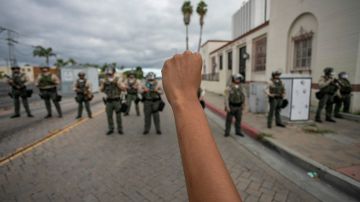 A person holds up a fist in front of a row of sheriff's deputies as relatives of Andres Guardado, who was shot and killed by a sheriff's deputy in Gardena, and activists rally to call on the city to rescind its policing contract, near the Compton Sheriff's Station in Compton, California, on June 28, 2020. (Photo by DAVID MCNEW / AFP) (Photo by DAVID MCNEW/AFP via Getty Images)