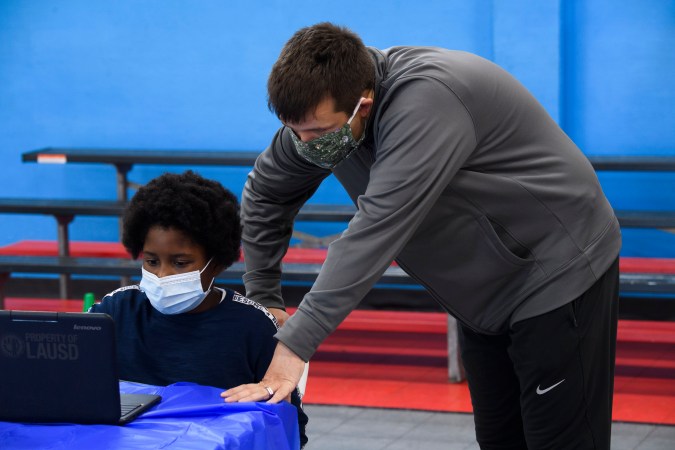 A YMCA staff member assists a child as they attend online classes at a learning hub inside the Crenshaw Family YMCA during the Covid-19 pandemic on February 17, 2021 in Los Angeles, California. - While many area schools remain closed for in-person classes, the learning hub program provides structured distance education resources including free WiFi, electricity, staff support, academic tutoring, and recreation activities to provide a safe environment to support low income and minority communities. (Photo by Patrick T. FALLON / AFP) (Photo by PATRICK T. FALLON/AFP via Getty Images)