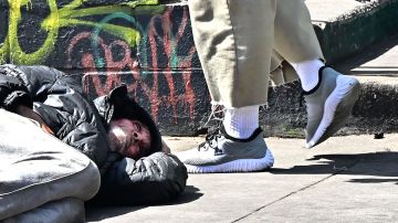 A pedestrian walks past a man sleeping on a Skid Row sidewalk on August 16, 2023 in Los Angeles, California, where homelessness has seen a 10 percent surge compared to last year. A recent report from the Los Angeles Homeless Services Authority reveals an estimate of 42,260 people living on the streets of Los Angeles without shelter, as the homeless population has more than doubled over the past decade. (Photo by Frederic J. BROWN / AFP) (Photo by FREDERIC J. BROWN/AFP via Getty Images)