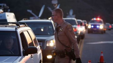 A California Highway Patrol officer checks the identifications of residents being allowing to pass through a roadblock on Highway 38 toward the Big Bear Lake, California as a standoff with the former Los Angeles police officer who is now-quadruple murder suspect Christopher Dorner continues, near San Bernardino, California February 12, 2013, some 46 miles (75 km) from the San Bernardino Mountains near Big Bear, California where Dorner, a former US cop, has barricaded himself in a cabin and exchanged gunfire with police who have the cabin surrounded. AFP PHOTO / David McNew (Photo credit should read DAVID MCNEW/AFP via Getty Images)