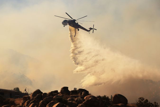 TOPSHOT - Water is dropped from a helicopter as the Highland Fire burns in Aguana, California, on October 31, 2023. Thousands of people were being told to flee a wildfire spreading in southern California on October 31, as strong winds fanned the flames. Around 5,700 people were urged to leave areas threatened by the blaze, which erupted on October 30 around lunchtime and had engulfed 2,200 acres (900 hectares) by the following morning. (Photo by DAVID SWANSON / AFP) (Photo by DAVID SWANSON/AFP via Getty Images)