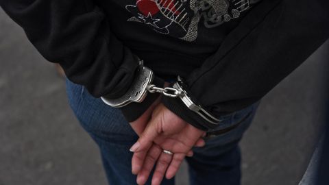 A handcuffed woman, part of a group of 72 alleged members the "Barrio 18" gang, waits to be registered by the National Civil Police after being arrested on charges of extortion and murder in Guatemala City on May 2, 2016. Security forces on Monday launched raids on one of the biggest gangs in Guatemala, arresting 72 suspected members in different parts of the country, officials said. / AFP PHOTO / JOHAN ORDONEZ (Photo credit should read JOHAN ORDONEZ/AFP via Getty Images)