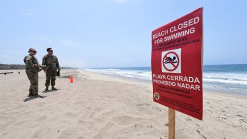 US Army National Guard members look at the water at Dockweiler State Beach in Playa del Rey, in Los Angeles County, California, on July 13, 2021, next to a sign indicating that the beach is closed to swimming after a sewage spill. 17 million gallons of sewage were discharged from the Hyperion Water Reclamation Plant one mile offshore, instead of the usual five miles, after the plant was "inundated with overwhelming quantities of debris", according to a statement released by LA Sanitation and Environment on July 12, 2021. (Photo by FREDERIC J. BROWN / AFP) (Photo by FREDERIC J. BROWN/AFP via Getty Images)