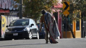 An unhoused person carries their blanket along Sunset Boulevard in Los Angeles, California, December 19, 2022. - A state of emergency over spiraling levels of homelessness was declared in Los Angeles on Monday as the new mayor pledged a "seismic shift" for one of the most intractable problems in America's second biggest city. Tens of thousands of people sleep rough on Los Angeles streets every night, in an epidemic that shocks many visitors to one of the wealthiest urban areas on the planet. (Photo by DAVID SWANSON / AFP) (Photo by DAVID SWANSON/AFP via Getty Images)