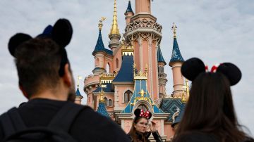 Visitors wearing emblematic Mickey and Minnie Mouse ears look on, in front of the Sleeping Beauty-inspired castle at Disneyland Paris, in Marne-la-Vallee, east of Paris, on October 16, 2023. The Walt Disney Company celebrates its 100th anniversary on October 16, marking the occasion with the release of a short film featuring more than 500 characters from 85 films. Disneyland Paris marked that anniversary with a parade showcasing a hundred of Disney's characters. (Photo by Ian LANGSDON / AFP) (Photo by IAN LANGSDON/AFP via Getty Images)