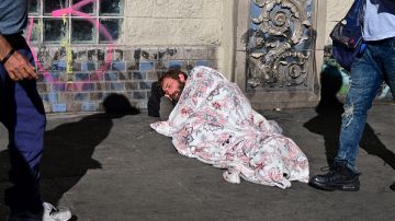 Pedestrians walk past a homeless man sleeping on the sidewalk on November 22, 2023 in Los Angeles, California, where skyrocketing rents in recent years has led to an increasing rise in the number of unhoused people. Some 75,500 people live on the streets of Los Angeles and its sprawling suburbs, according to a January survey. The figure is up 70 percent since 2015, in a city where sometimes shocking levels of inequality are on daily display. (Photo by Frederic J. BROWN / AFP) (Photo by FREDERIC J. BROWN/AFP via Getty Images)