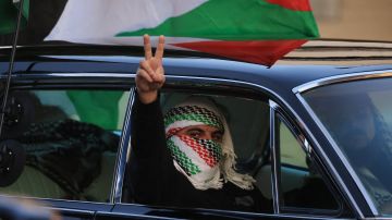 A passenger wearing a keffiyeh gestures a V sign as pro-Palestinian protesters rally during the "Black & Palestinian Solidarity for a Ceasefire this Xmas" by the Beverly Center shopping center in Los Angeles on December 23, 2023. More than 200 people were killed in 24 hours of Israeli strikes, Gaza officials said December 23, and Israel announced the death of five soldiers after the UN failed to call for a ceasefire. Eleven weeks into the Israel-Hamas war, Israeli forces pressed on with their offensive, a day after the UN Security Council adopted a resolution for more aid to flow into the besieged Gaza Strip. (Photo by DAVID SWANSON / AFP) (Photo by DAVID SWANSON/AFP via Getty Images)