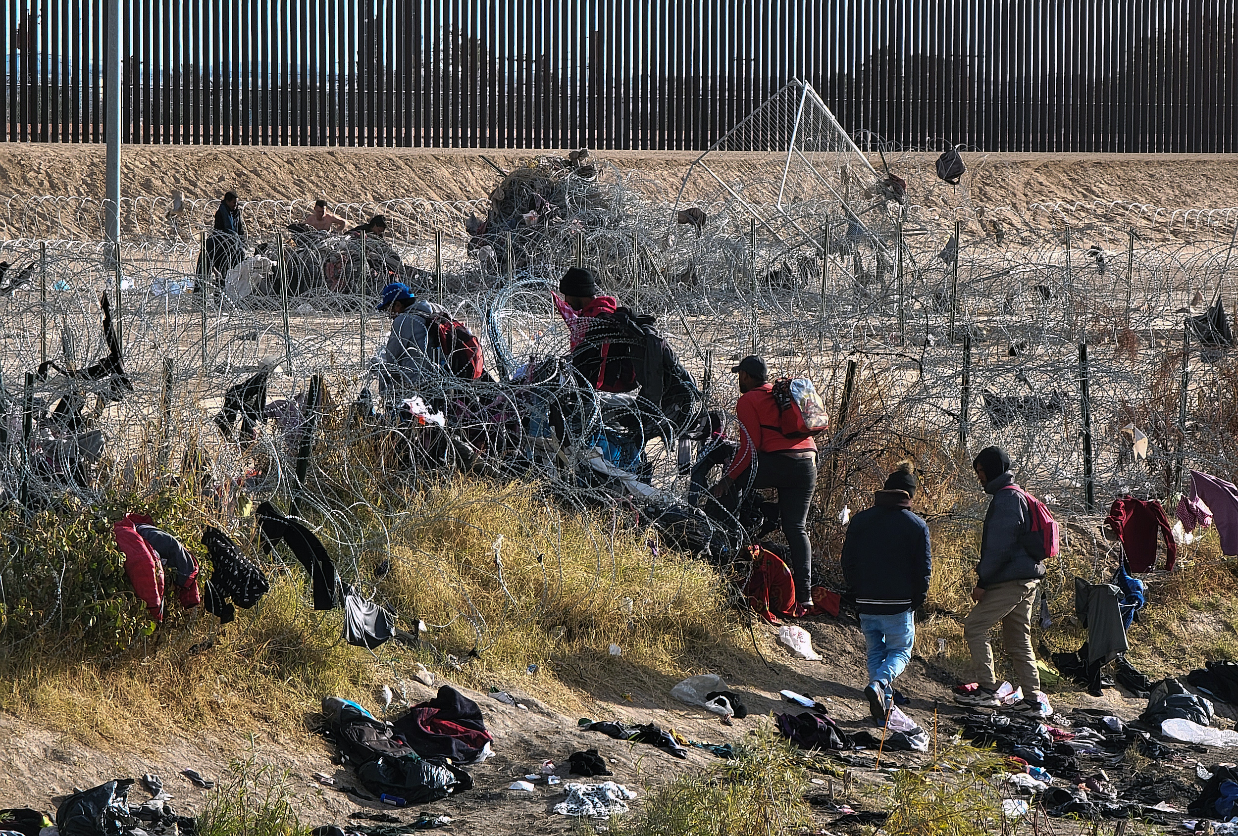 Migrantes cruzan la cerca de púas cerca del muro fronterizo en Texas para entregarse a las autoridades de Estados Unidos.