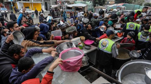 Los refugiados palestinos sostienen cuencos vacíos mientras intentan alcanzar los alimentos distribuidos por voluntarios en Rafah.