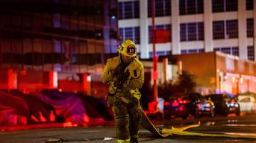 A firefighter drags a hose on San Pedro Street after a fire in a single-story commercial building sparked an explosion in the Toy District of downtown Los Angeles on May 16, 2020. - At least 11 firefighters were injured in downtown Los Angeles when a fire in a commercial building sparked a major explosion and spread to nearby structures, fire officials said. Some 230 responders battled the blaze as it spread to other buildings in the area before it was extinguished around two hours after it began. (Photo by Apu GOMES / AFP) (Photo by APU GOMES/AFP via Getty Images)