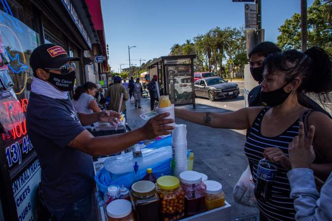 A street vendor sells a snow cone to customers in MacArthur Park, Los Angeles on May 21, 2020. - Undocumented immigrants impacted by the corornavirus shutdown can apply for California coronavirus emergency assistance plan for undocumented people put in place by Governor Gavin Newsom in April. (Photo by Apu GOMES / AFP) (Photo by APU GOMES/AFP via Getty Images)